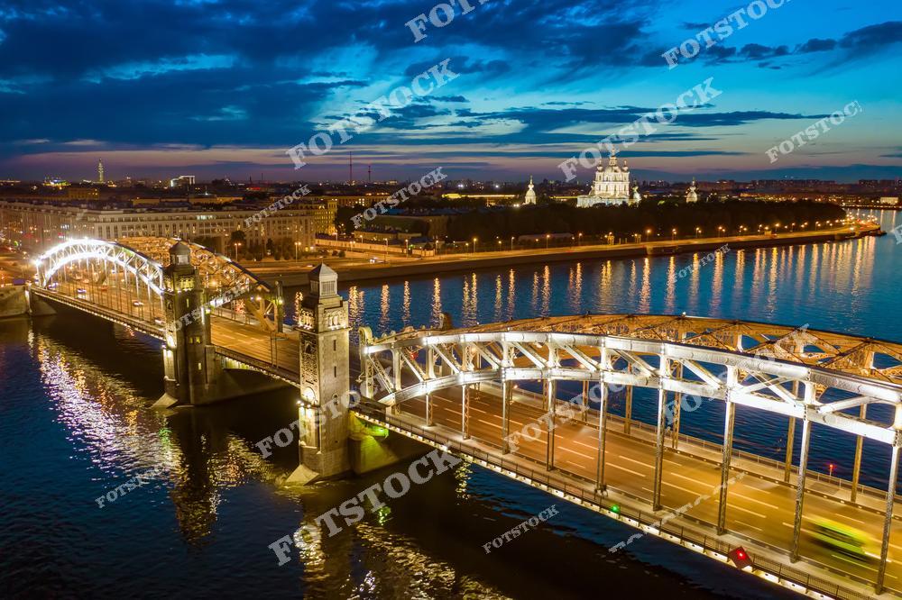 На фотографии изображен Казанский собор на Невском проспекте в Санкт-Петербурге, величественно освещенный на фоне закатного неба. Его колоннада и купол подсвечены, выделяясь среди городской застройки и подчеркивая монументальность архитектуры. Закатные цвета придают сцене драматичность и особое очарование, подчёркивая красоту ночного Петербурга. Этот собор является одним из главных символов города на Неве.